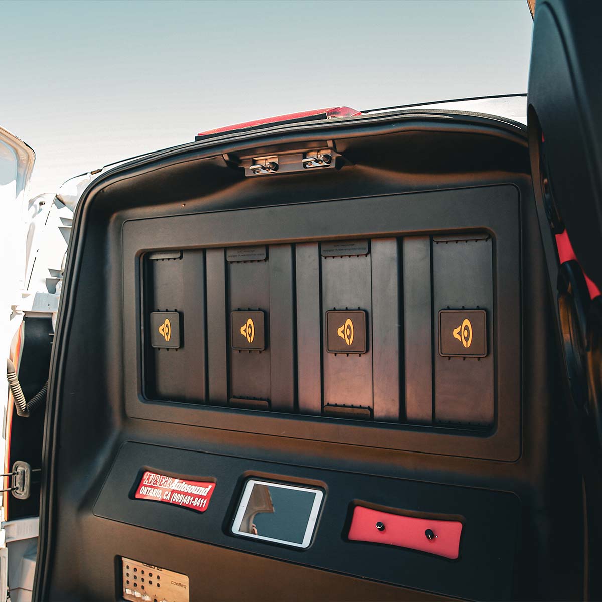 An open vehicle trunk shows four secure compartments with yellow speaker icons, perfect for SPL enthusiasts. Featuring a Cerwin Vega Stroker Pro 1600W RMS Class-D Mono Amplifier, it has control buttons, a small screen, and a red and white safety warning label on the left side.