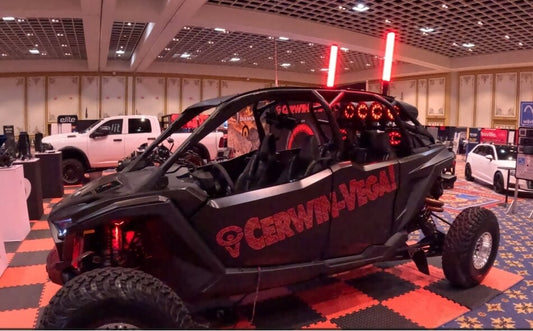 A custom black UTV with Cerwin-Vega branding featuring multiple red LED-lit tower speakers mounted on the roll cage at an automotive event.