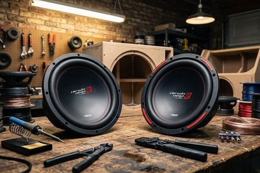 A professional car audio workshop setting featuring two Cerwin-Vega 12-inch subwoofers, the H7124D and XED12V2
