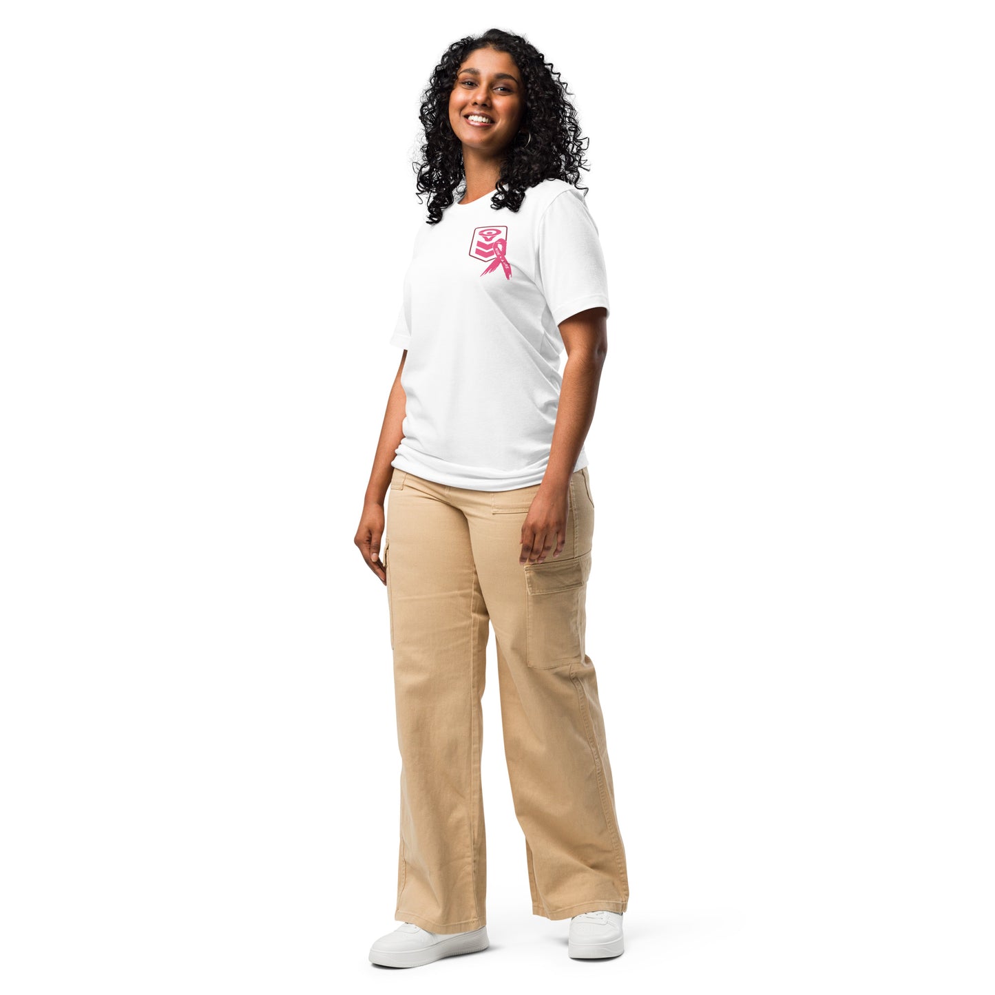 A person with curly hair smiles while facing forward, wearing the Cerwin-Vega Breast Cancer Awareness T-Shirt and beige cargo pants. They stand relaxed, hands by their sides, promoting breast cancer awareness. White sneakers complete the casual look against a plain white background.